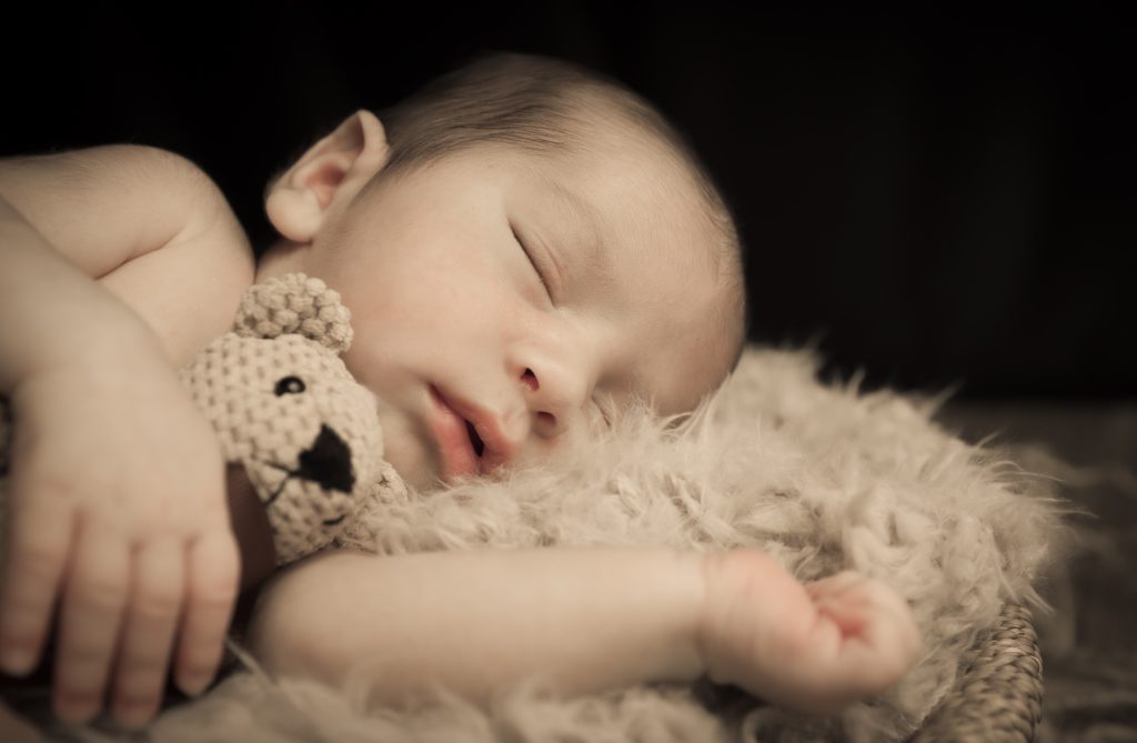 Bebé recién nacido durmiendo abrazado a un osito durante una sesión newborn en Murcia.